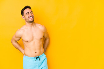 Young caucasian man with swimsuit isolated on yellow background Young caucasian man with trrelaxed and happy laughing, neck stretched showing teeth.