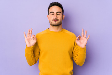 Fototapeta premium Young caucasian man isolated on purple background relaxes after hard working day, she is performing yoga.