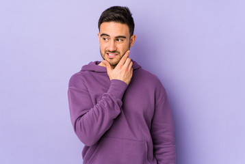 Fototapeta premium Young caucasian man isolated on purple background touching back of head, thinking and making a choice.