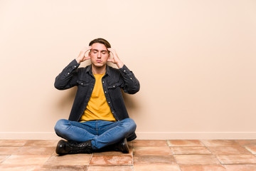 Young caucasian man sitting on the floor isolated touching temples and having headache.
