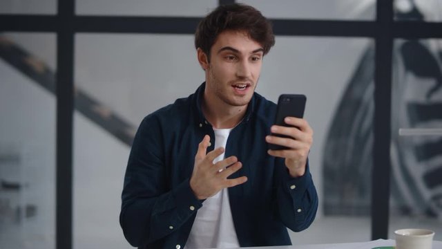 Smiling business man making video call on smartphone in office.
