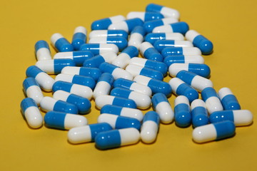 Double colored white and blue capsules tablets pills on yellow background macro 