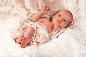 A baby boy is peacefully sleeping during his first professional photo shoot. He is dressed in white and covered with a white blanke