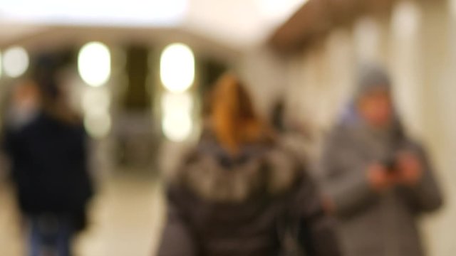 Girl in winter jacket looks at camera then turns sharply and leaves in lobby of metro station in Moscow, Russia. Young beautiful woman resentfully walks away from viewer through hall of subway station
