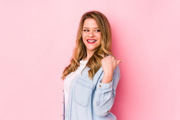 Fototapeta premium Young caucasian woman isolated on pink background points with thumb finger away, laughing and carefree.
