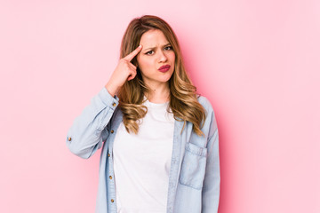 Obraz premium Young caucasian woman isolated on pink background pointing temple with finger, thinking, focused on a task.