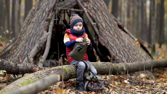 Little boy scout during hiking in autumn forest. Child packs a backpack near a teepee in the woods. Concepts of adventure, scouting and hiking tourism for kids.