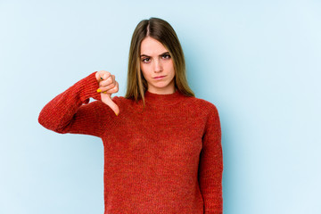 Young caucasian woman isolated on blue background showing a dislike gesture, thumbs down....