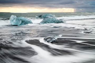 Iceberg on the black beach and white wave captured with long exposure