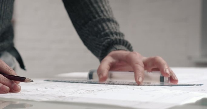 Close up of Middle Aged Architects Hands making important Blueprints at his Office. Using ruler and Pencil. Working with Calculations and making Lines on the Large format Paper.