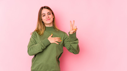 Young caucasian woman isolated on pink background taking an oath, putting hand on chest.