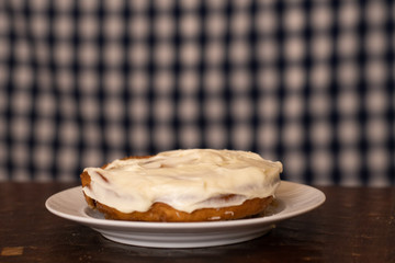 A cream cheese frosted cinnamon roll on a dish with a blue and white background. 