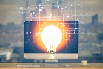Computer on desktop in office with bulb icon hologram. Multi exposure. Concept of idea.