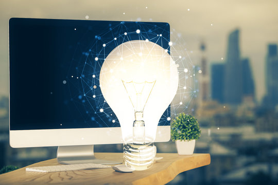 Computer on desktop in office with bulb icon hologram. Multi exposure. Concept of idea.