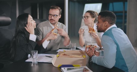 Cheerful coworkers eating lunch and relaxing in board room