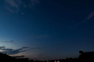 Bright iridium communication satellite flare at sunset above city houses