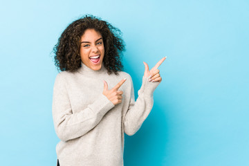 Young african american curly hair woman pointing with forefingers to a copy space, expressing...