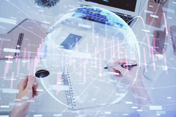Hands writing information about stock market in notepad. Forex chart holograms in front. Concept of research. Multi exposure