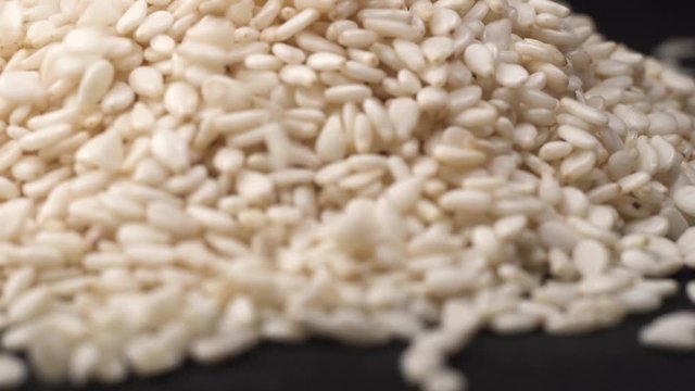 Fresh raw white sesame seeds falls on spinning black table in kitchen with black background. Cooking concept with sesame seeds topping.