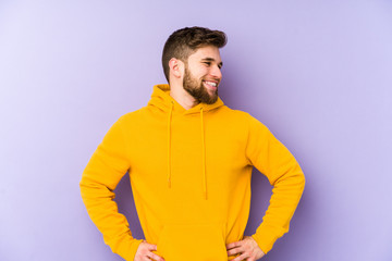 Young man isolated on purple background confident keeping hands on hips.