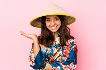 Young mixed race hispanic woman isolated showing a copy space on a palm and holding another hand on waist.