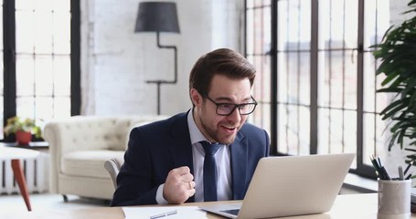 Overjoyed professional businessman executive celebrates online project business success receiving good news in email. Euphoric man entrepreneur triumphant looks at laptop rejoices victory achievement.