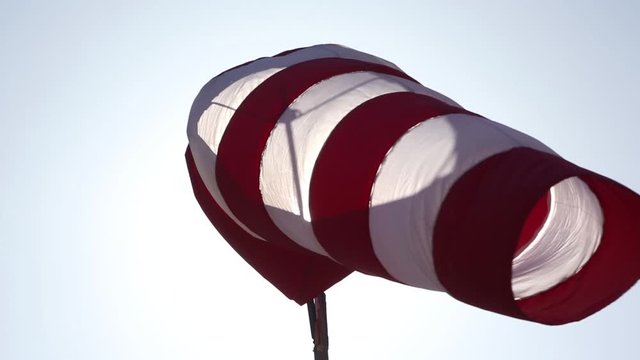 Red and white windsock blowing in wind with sun shining through lens flare