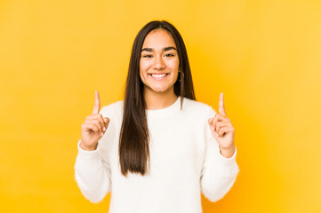 Young woman isolated on a yellow background indicates with both fore fingers up showing a blank...