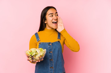 Young asian woman holding a salad isolated shouting and holding palm near opened mouth.