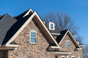 Pointed  gable roofs with attic windows on a house covered with manufactured veneer stone blue sky background