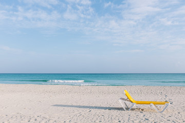 Abandoned yellow resort chair on idyllic empty beach with calm turquoise water in Varadero, Cuba