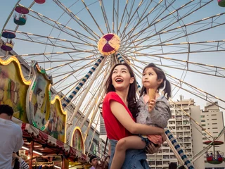 Foto op Plexiglas gelukkige azië moeder en dochter hebben plezier in amusementscarnavalpark met farris-wiel en carrouselachtergrond © anusak