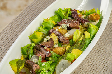 Rustic green salad with meat, potatoes and avocado, restaurant meal.