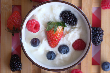 Bowl of blueberries, strawberry and yogurt on wooden table.