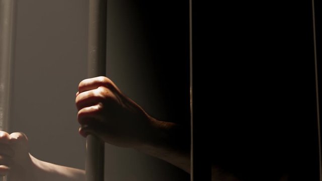 Hands gripping prison bars in hazy dramatic light