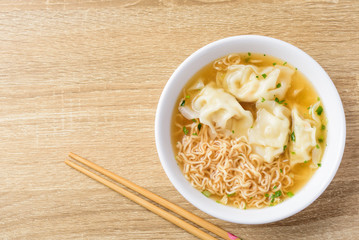 Instant noodles soup and wonton dumpling stuffed with minced pork in a bowl and chopsticks on  wooden background, Asian food, Top view