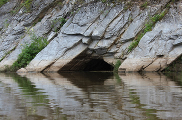 A cave in the rocks, flooded with water. Stone rocks and their reflection, Belaya river, Russia, South Ural. Traveling on the Agidel River, Bashkortostan