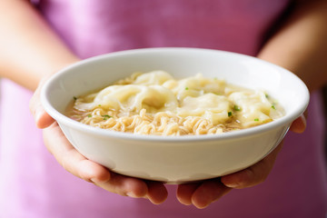 Instant noodles soup and wonton dumpling stuffed with minced pork in a bowl holding by hand, Asian food