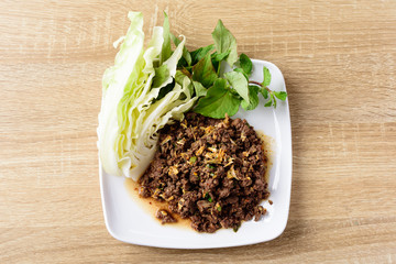 Local Northern Thai food, spicy minced pork salad (Larb Moo Kua) eating with fresh vegetables on wooden background, top view