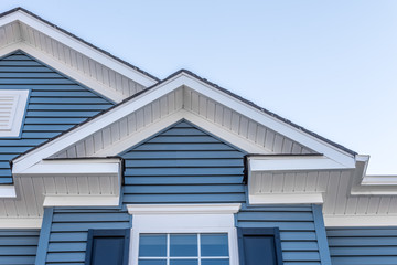 Decorative gable roof with white cornice, blue horizontal vinyl siding with light blue sky - obrazy, fototapety, plakaty