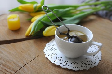 Spring morning. A cup of green tea with yellow tulips on wooden table