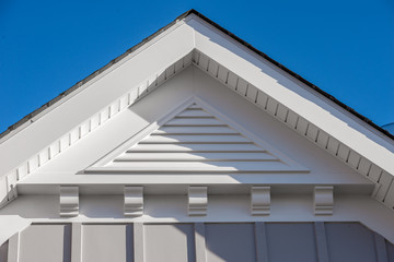 Close-up view of a white PVC triangle gable vent above a decorative trim board on a newly built...