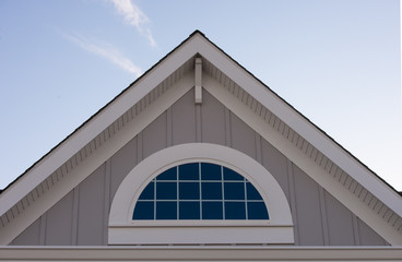 Half round decorative attic window with white grilles on desert tan vertical lap vinyl siding,...