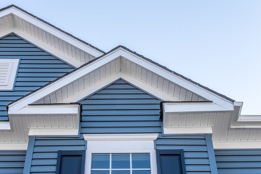 Decorative gable roof with white cornice, blue horizontal vinyl siding with light blue sky