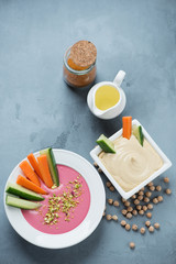 Fototapeta na wymiar Hummus with carrot and cucumber slices over grey concrete background, vertical shot, view from above