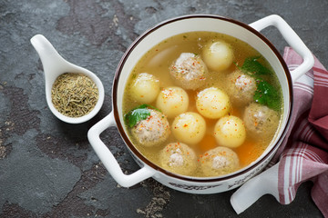 Bowl of soup with meatballs and potato balls, studio shot over brown stone background