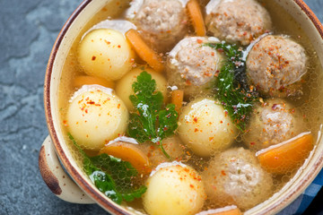 Close-up of soup with meatballs, potato balls, carrots and greens served in a beige bowl, selective focus
