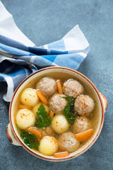Meatball and potato soup served in a beige bowl, top view on a blue stone background, vertical shot with space