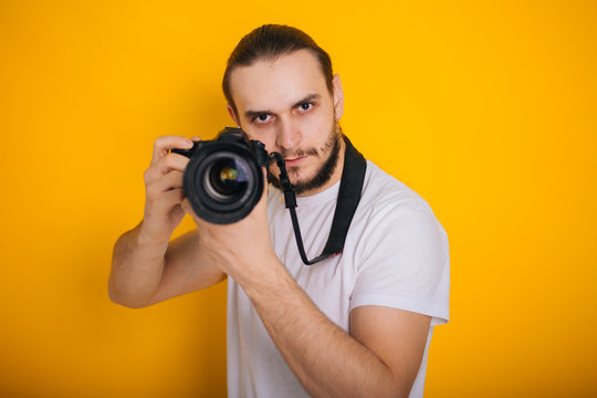 Photographer on a yellow background. The guy is looking into the viewfinder of the camera. Process work. Photographs in the studio