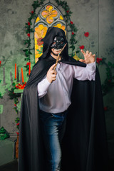 A guy in a black mask in the form of a skull and in a black cloak. Evil sorcerer with a magic wand....